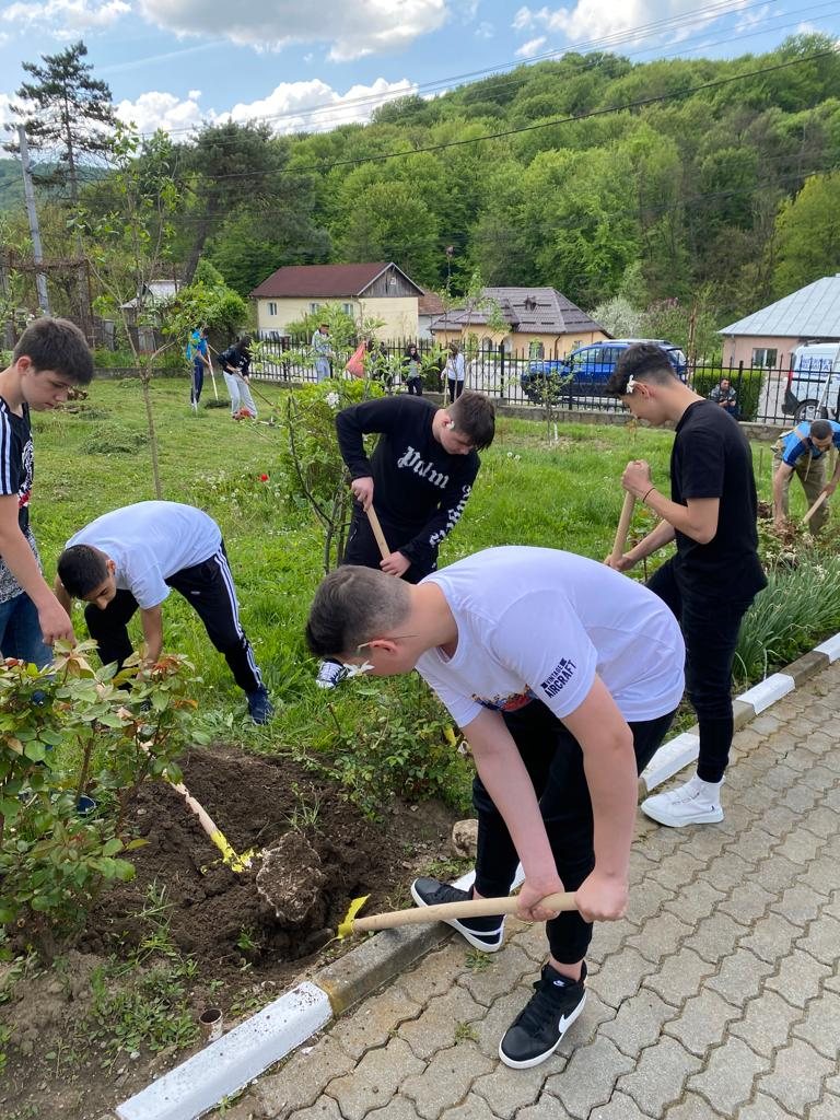 Mai mulți tineri sapă și plantează flori într-o curte, contribuind la amenajarea spațiului